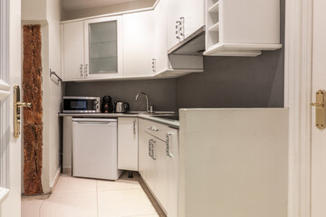 corner of a kitchen with white wooden cabinets, a glass cabinet, a gray countertop, a small white fridge and a microwave coffee maker and oven, a kettle on the counter