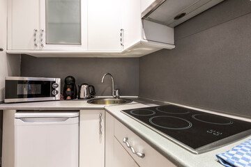 Fototapeta premium corner of a kitchen with white wooden cabinets, a display cabinet, a gray countertop, a small white fridge and a coffee maker and a microwave oven, a range hood and a kettle on the counter