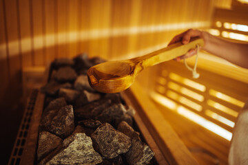 Woman in Finnish sauna, holding wooden sauna bucket. Woman is pouring water into hot stone in Sauna...