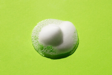 Foam on a green background. Soapy liquid texture with bubbles. Natural sunshine and shadows. Skin care cleansing cosmetic in top view.