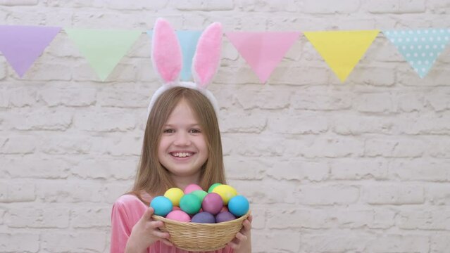 Portrait of funny Easter child wearing bunny ears with colorful eggs. Pretty little girl having fun in springtime in decorated room. Cute kid smiling