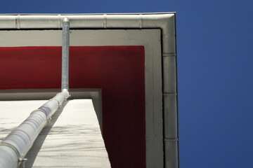 Very steep angle view under red painted gable and rain gutter under blue sky (horizontal),...