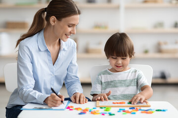 Professional woman language teacher exercising with preschooler, little boy making word with letters, free space