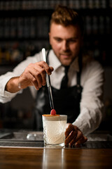 Fototapeta na wymiar male hand holding tweezers and carefully put raspberry on glass with cocktail