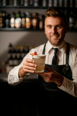 selective focus on glass with tasty foamy cocktail decorated with orange slice and a raspberry in male hands