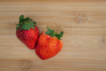 A couple of delicious red strawberries on a cutting board. Over view, over head photo. Point of view. 