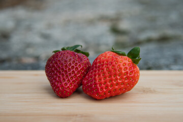 A couple of delicious red strawberries on a cutting board in the garden. Vibrant colors.