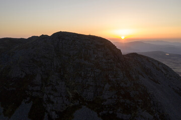 Wide aerial view of a man stood upon a mountain at sunrise