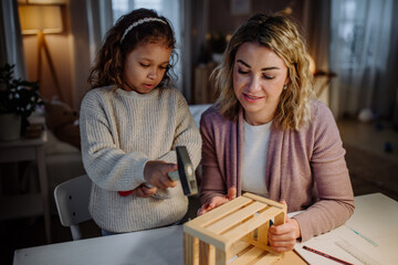 Happy little girl renovating a wooden crate together with her mother at home.