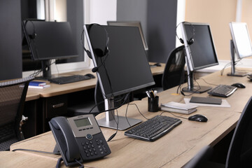 Modern computers with headsets and stationary phone on wooden desk in office. Hotline service