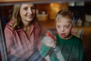 Boy with Down syndrome with his mother cleaning window at home.