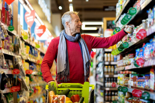 Cheerful elderly man choosing sauce at supermarket