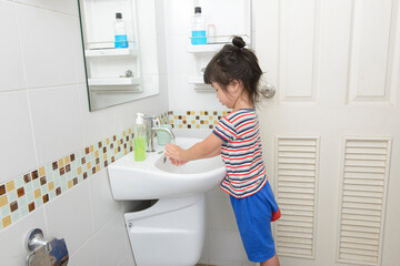 Little Asian girls wash their hands in the bathroom.