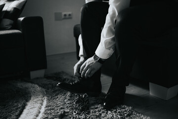 Groom tying his shoes preparing for the wedding in grayscale