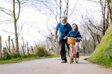 Grandfather teaching girl riding bicycle in countryside