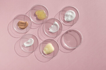 Multicolored textures of cream, scrub, serum and oil in Petri dishes on a pink background. Concept of cosmetics laboratory researches. Smear of skincare cosmetics product. Wellness and beauty concept.