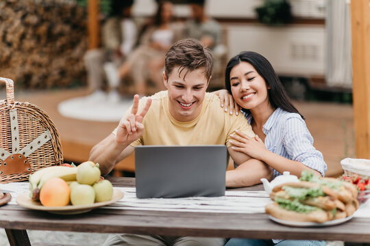 Millennial diverse couple using laptop computer near motorhome, video chatting online on summer camping trip
