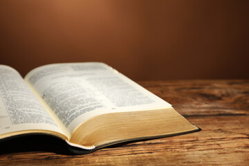 Open Bible on wooden table against brown background, closeup. Christian religious book