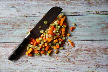 Vegetables, organic, raw, cut very small. Carrot, pumpkin and chayote, with knife on wooden table, isolated.