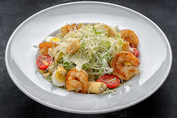 Caesar salad with shrimps, on a dark background.