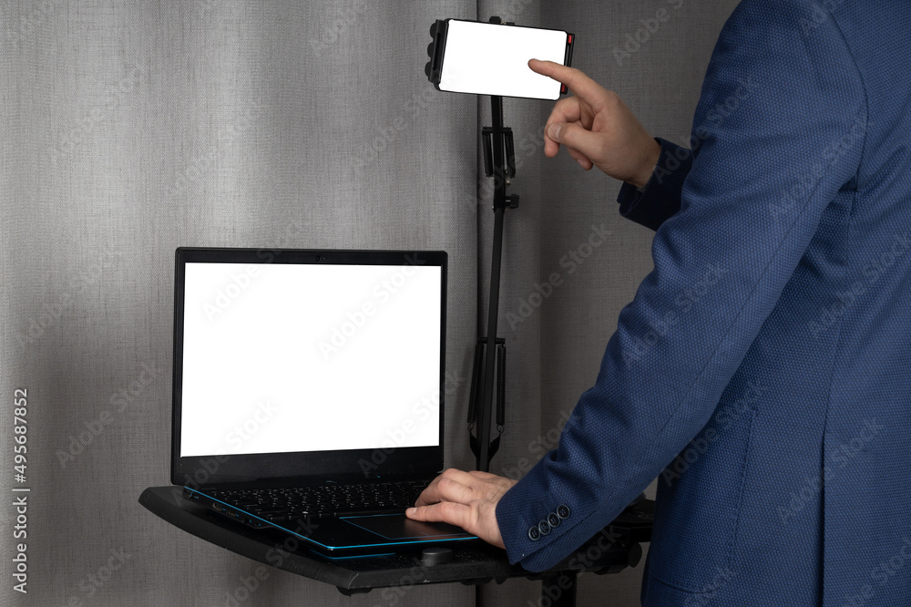 Poster person in a suit standing in front of the laptop and using the smartphone on a tripod