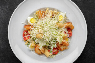 Caesar salad with shrimps, on a dark background.