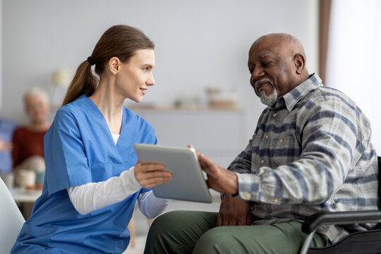 Friendly nurse helping black senior man using digital tablet