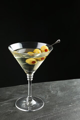Martini cocktail with olives on grey table against dark background