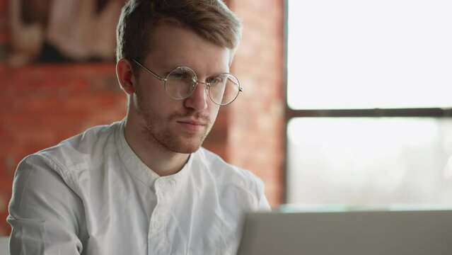 handsome serious man is typing text on laptop, working remotely in cafe, closeup portrait of face with glasses