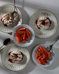 Italian dessert panna cotta with fruits jam and fresh pieces of strawberries on plates. Top view