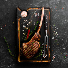 Bone steak. Tomahawk steak on a black wooden background. Top view. Free space for text.