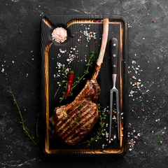  Bone steak. Tomahawk steak on a black wooden background. Top view. Free space for text. © Yaruniv-Studio