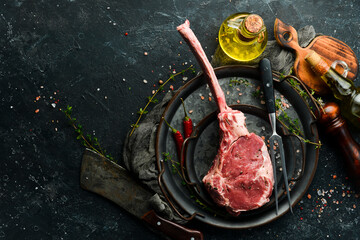 Dry aged raw tomahawk beef steak with ingredients on a black stone background. Top view. Flat Lay.