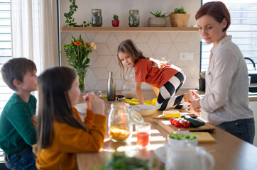 Mother of three little children preparing breakfast in kitchen at home.