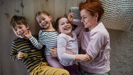 Top view of cheerful mother with three little children lying on floor together at home.