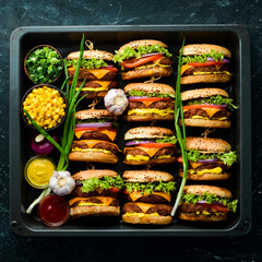 Delicious grilled homemade burgers with beef, tomatoes, cheese, onions and salad. Burger menu. Top view. On a black stone background.