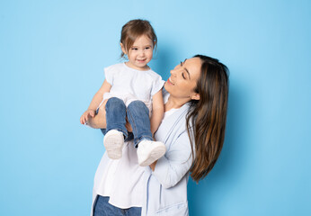 Photo of pretty young mommy hugging little daughter standing isolated over blue background....