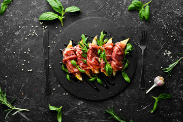 Prosciutto with pear and basil on a black stone plate. Jamon. Italian antipasto. Top view.