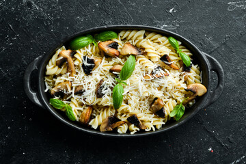 Pasta with mushrooms, parmesan cheese and basil in a black pan. Top view.