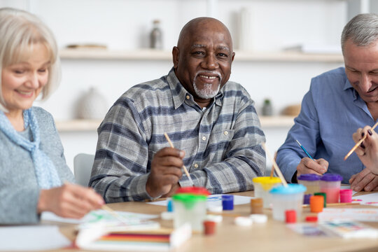 Happy senior black man enjoying painting activity with his friends
