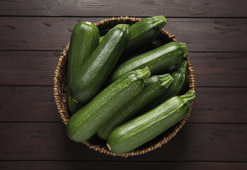 Raw ripe zucchinis in wicker bowl on wooden table, top view