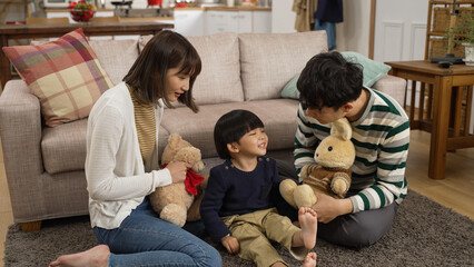 slow motion of asian dad, mom and baby son playing with toy animals on living room floor at home. the man uses stuffed bunny’s hand to touch cute son’s face