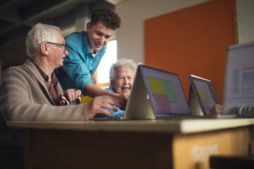 Senior group in retirement home with young instructor learning together in computer class