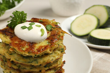 Delicious zucchini fritters with sour cream on plate, closeup. Space for text