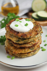 Delicious zucchini pancakes with sour cream served on white wooden table, closeup