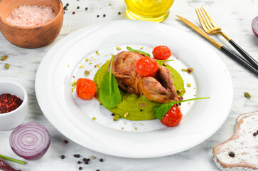 Baked quail in bacon with spinach hummus on a white plate. Top view. Rustic style.
