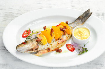 Baked sea bass with oranges and vegetables on a white plate. Top view. Rustic style.