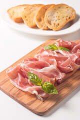 Closeup of thin slices of prosciutto with mixed olives and paprika on wooden cutting board