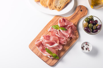 Closeup of thin slices of prosciutto with mixed olives and paprika on wooden cutting board