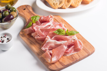 Closeup of thin slices of prosciutto with mixed olives and paprika on wooden cutting board